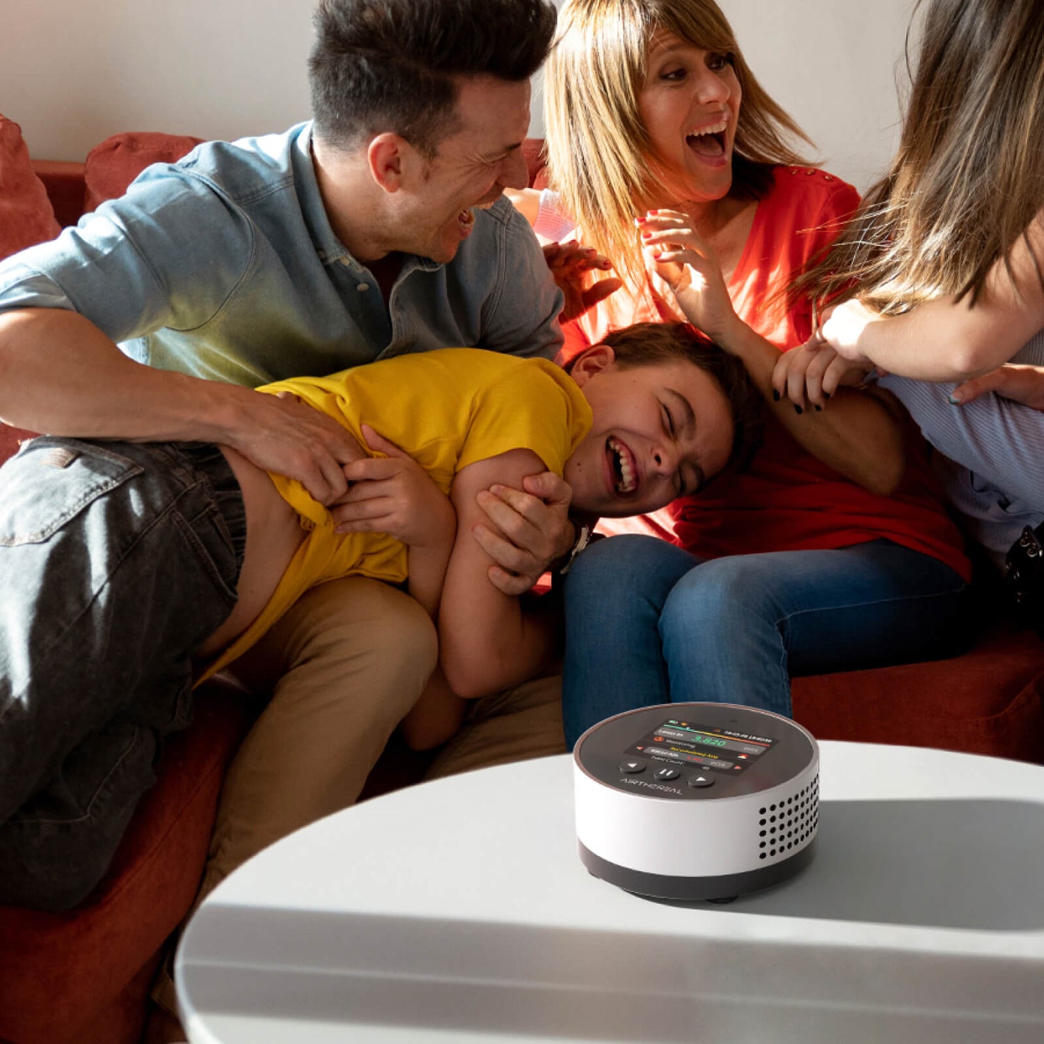 Family laughing on couch with Airthereal radon detector on table.