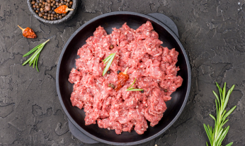 ハーブで飾られた生の挽き肉のボウルが、暗い表面の上に全体のスパイスに囲まれています。