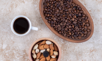コーヒー豆が入った皿と、ナッツが盛られたボウル、黒いコーヒーのカップ。