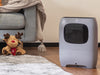 A gray vacuum next to a plush reindeer toy on a rug. Cozy living room setting.